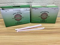 Two green and white boxes labeled GEN-MARK International Distribution USA containing red giant straws, and two individual straws displayed in front of the boxes.