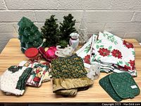 Photo showing all Christmas-themed items including decorative trees, linens, a penguin figurine, and holiday fabric items on a table.