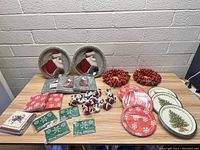 Photo showing two Santa Claus decorative plates, two red berry wreaths, assorted Christmas napkins, multiple Santa figurines, and Christmas-themed coasters on a wooden table.