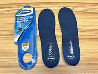 Photo of Dr. Scholl's Energizing Comfort massaging gel insoles for men alongside original packaging on wooden surface.