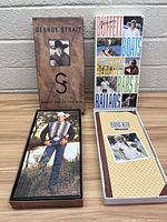 Both George Strait and Jimmy Buffett CD box sets standing upright against a wall displaying front covers