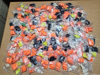 Multiple individually bagged sets of fake nails in orange, black, yellow, and clear colors spread on a flat surface.