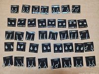 Overview of 39 pairs of new rhinestone earrings on Madeline branded black cards arranged in rows on flat tan surface showing variety of styles and sizes.