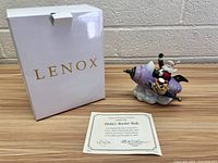 Lenox Santa's Rocket Ride 2003 figurine displayed with original white Lenox box and certificate of authenticity on wood surface against a brick wall.