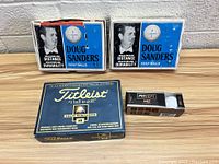 Two boxes of Doug Sanders golf balls, one box of Titleist golf balls and one box of Precept golf balls displayed on a wooden surface.