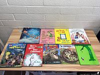Top down view of 9 children's books arranged on a wooden table, featuring colorful covers with Christmas, dinosaur, and classic children's story themes.