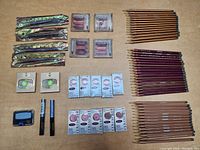 Full lot overview photo showing large quantity of various make-up items including eye shadow, mascaras, liners, and pencils on wooden surface.