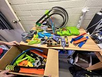 Wide view showing assorted Mario Kart Hot Wheels track parts, various colors and pieces on wooden table, with box containing more parts open below