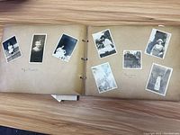 Open photo album showing multiple black and white photos of individuals on two pages, some photos tilted and some with handwriting captions below images