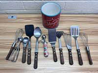 Complete set of utensils and red metal utensil holder shown laid out on wood surface.