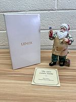 Photo of 2001 Lenox Santa figurine, original box, and certificate displayed on floor against wall.