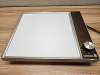 Front view of vintage Corning hot plate showing white ceramic heating surface and wood-grain control panel with knob
