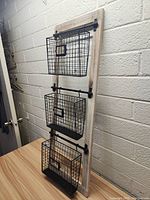 Front view of the wall hanging organizer showing all three black metal wire baskets on the distressed wooden board.