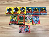 Eleven assorted vintage wax packs laid flat on wooden surface showing various trading card series including Dick Tracy, Robin Hood, Rocketeer, Dinosaurs Attack, The Andy Griffith Show, and Rambo.