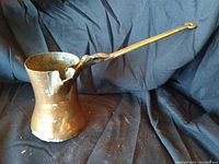 Side view showing large copper ladle with long handle and visible damaged spout area.