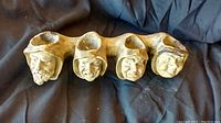 Antique ceramic pipe rack showing four individual sculpted faces to hold pipes, sitting on a black cloth.