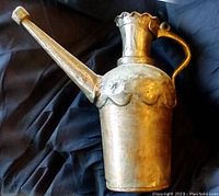 Full view of antique metal pitcher with an elongated spout, handle, and decorative scalloped pattern near neck.