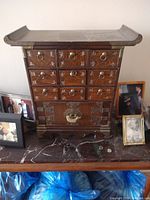 Front view of wooden cabinet with multiple small drawers, brass ring pulls, brass latch on bottom compartment, pagoda-style curved top
