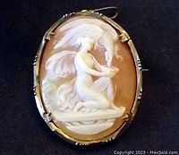 Front view of oval shell cameo brooch showing carved figure and metal frame