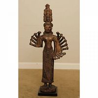 Front view of the tall Buddhist sculpture showing the multiple arms, hand details, long garment, and detailed headdress with stacked faces.