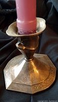 Metal candle holder with octagonal base and flared candle cup holding a pink candle.