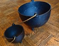 Large and one small cast iron bowl on wooden floor showing shape, legs and brass handle