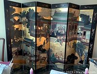 Front view of six-panel folding room divider showing detailed traditional Chinese figures and architectural scenes in warm colors on a lacquered black background.