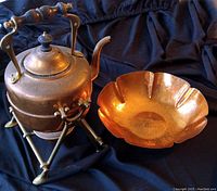 Copper kettle and bowl shown together on a black cloth background.