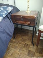Side view of first wooden end table next to couch showing wood top, drawer, and steel legs.