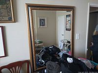 Photo shows a large rectangular mirror with a decorative gold frame hanging on a wall. The mirror measures approximately 36 inches by 46 inches. The reflective surface is clean and undamaged. The frame has a vintage ornate design.