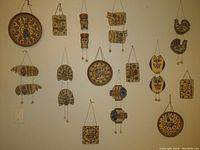Full view of 19 hanging pottery pieces arranged on a white wall, showing various animal and abstract designs in natural and blue tones.
