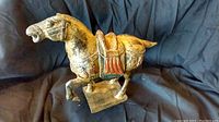 Photo of pottery horse figurine approximately 8 inches tall, depicting it standing on a mounted base with saddle and bridle detail.