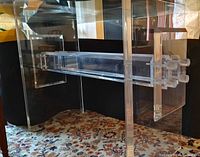 Side angle showing Lucite base structure with rectangular legs and horizontal crossbars on a patterned rug.