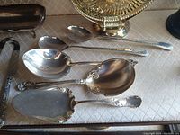 Silver plated assorted serving spoons, ladle, and pie server on a table.