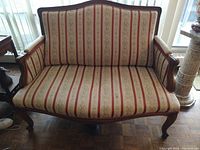 Front view of Victorian sofa showing carved walnut frame with cream, red, and beige striped floral fabric upholstery.