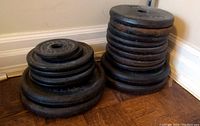 Two stacks of cast iron weight plates of various sizes on wooden flooring near a white baseboard.