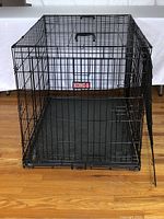 Front view of the black KONG wire pet crate with one door open, showing the metal grid and black plastic tray base.