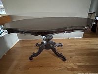 View of the scalloped edged wooden dining table top and pedestal base from the front.