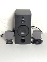 Full view of the Harman Kardon speakers including two small satellite speakers and one large subwoofer speaker on white background.