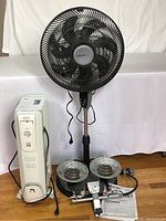 Full lot view showing DeLonghi heater, Comfort Mate fan, and Remington propane top heater with hose and parts spread on floor
