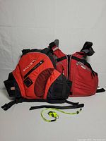 Two kayak life jackets side-by-side: Salus red vest with mesh pockets and Stohlquist red vest, shown fully visible from the front.