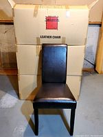 Assembled chair in front of stacked boxes labeled 'Leather Chair' with red Van Leuwen logo