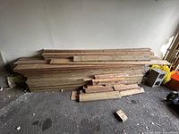 Large stack of long wood boards and planks against garage wall