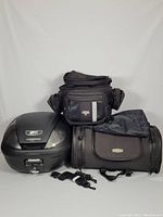 Photo of the entire motorcycle travel lot including the Givi hard case, Nelson Rigg expandable bag, Kuryakyn bag with waterproof cover, and two detachable straps arranged on a white background.