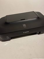 Canon iP2702 printer showing top view with paper input tray closed and Canon logo on front.