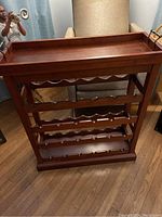 Front view of cherry wood wine rack showing four shelves with carved bottle holders and raised top surface.