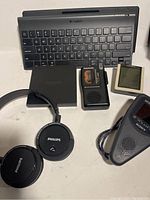 Overview of the lot items including Logitech keyboard, Amazon Fire box, Philips Bluetooth headphones, digital devices.