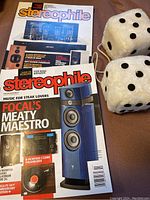 Two Stereophile magazines with audio equipment on covers and two fuzzy dice on a fabric surface.