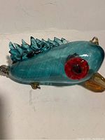 Side view of the glass fish ornament showing translucent blue-green body and red-black eye.