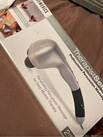 Top view of the unopened original box showing the product image of the percussion massager indicating its purpose for deep muscle therapy.